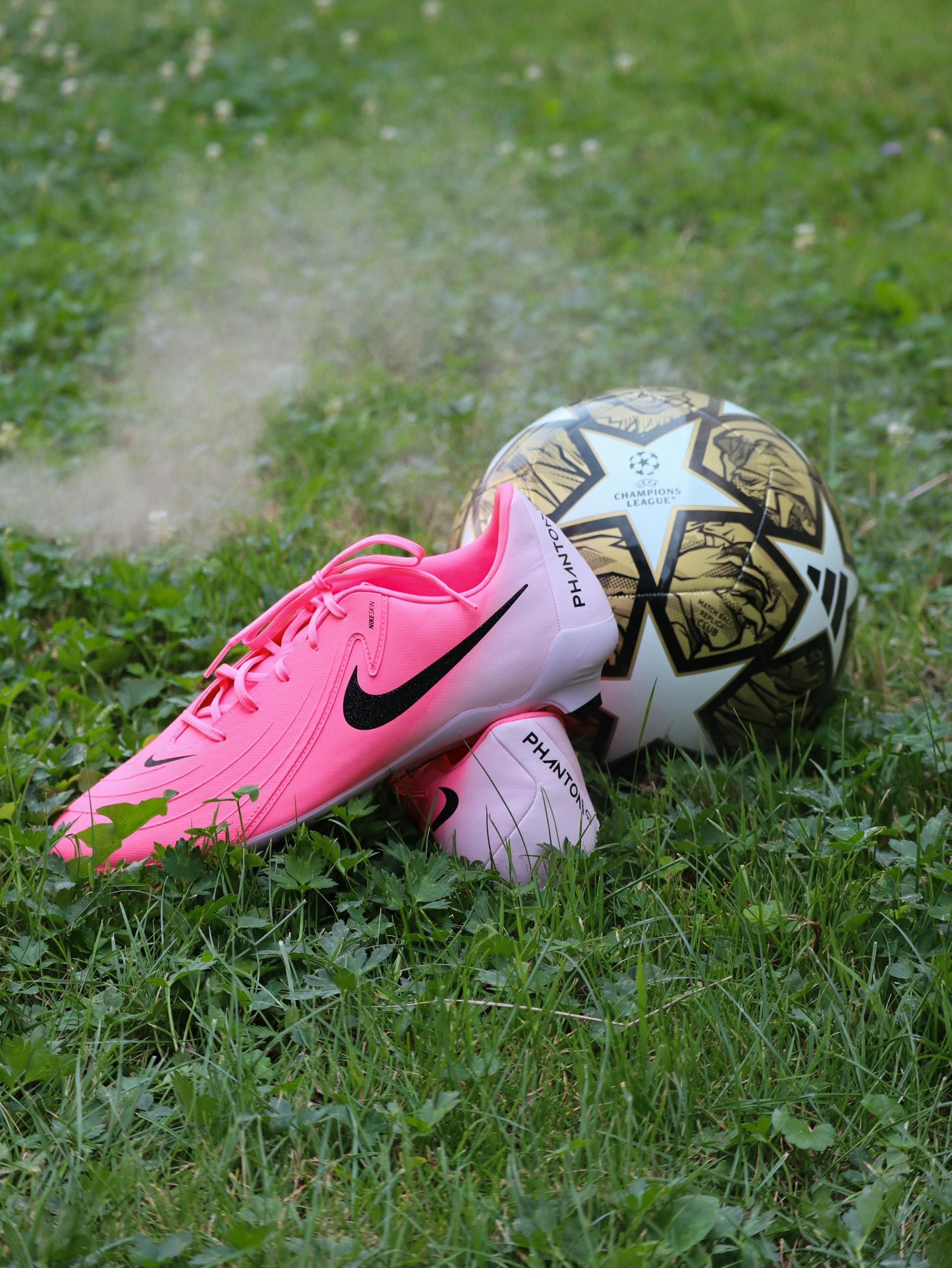 Bright pink soccer cleats and ball on lush grass; perfect for sports themes.